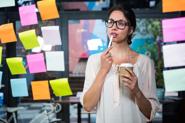 Donna di affari che esamina nota appiccicosa e che beve caffè