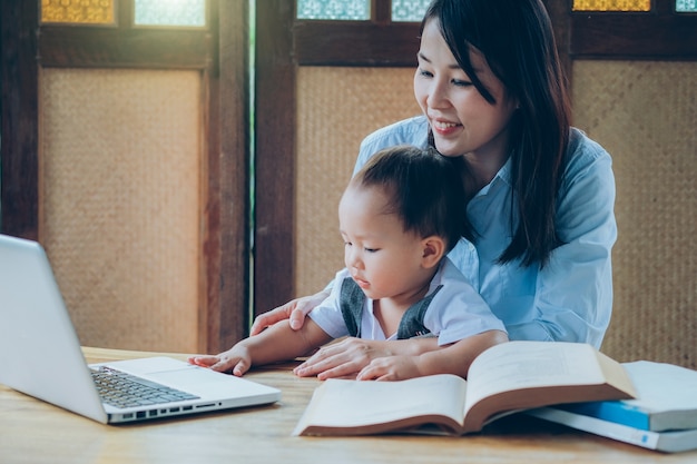 Donna di affari che insegna al suo bambino con multimedia e libro, scuola domestica.