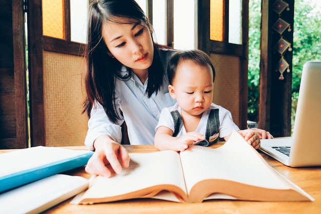 Donna di affari che insegna al suo bambino con multimedia e libro, scuola domestica.