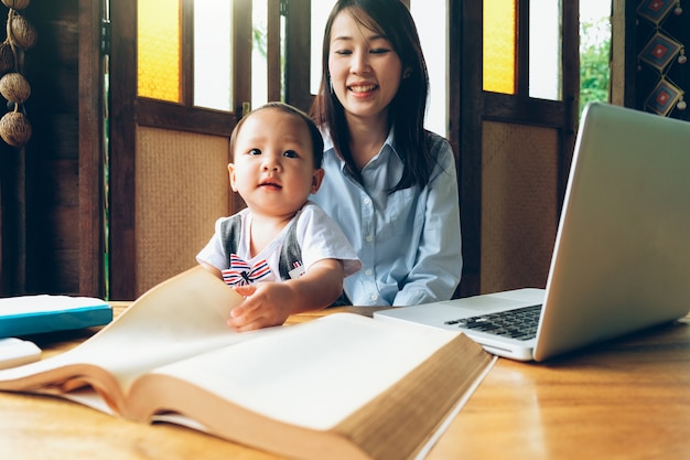 Donna di affari che insegna al suo bambino con multimedia e libro, scuola domestica.