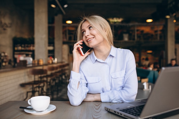 Donna di affari che lavora al computer portatile e al telefono in un caffè