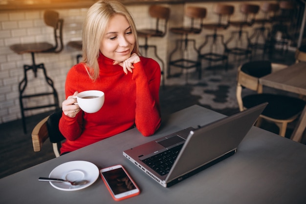 Donna di affari che lavora al computer portatile e che beve caffè in un caffè