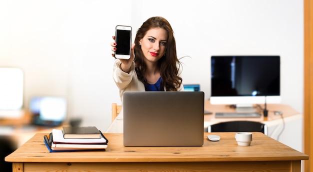 Donna di affari che lavora con il suo computer portatile e con il suo cellulare nell&#39;ufficio