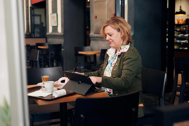 Donna di affari che lavora dalla caffetteria con un tablet e un taccuino