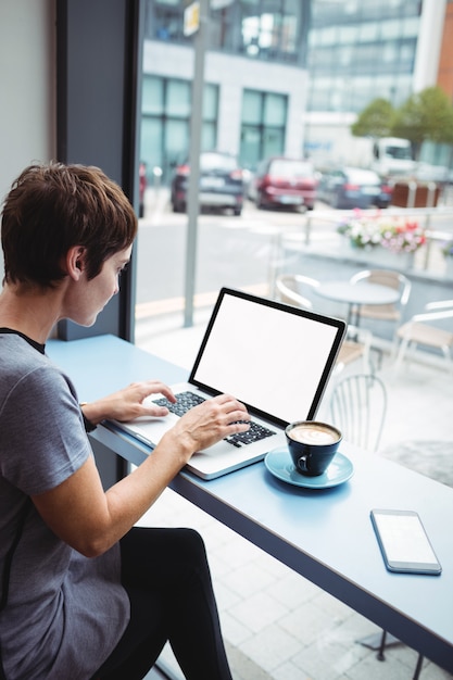 Donna di affari che mangia un caffè del od della tazza mentre per mezzo del computer portatile