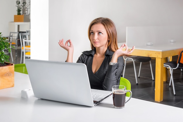 Donna di affari che medita vicino al computer portatile. Impiegato di concetto rilassato che fa meditazione di yoga durante una pausa caffè