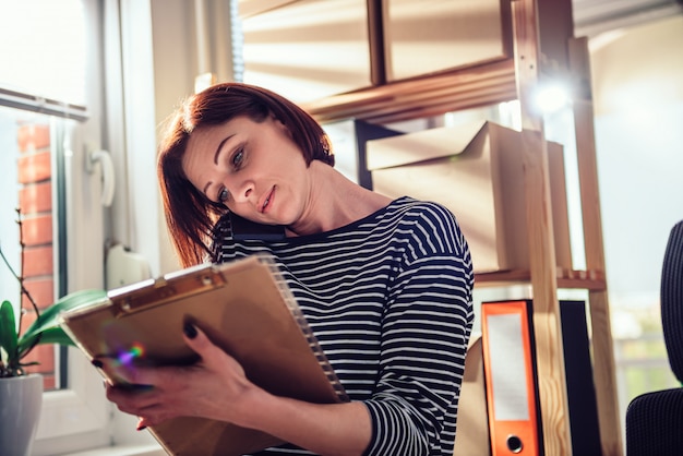 Donna di affari che parla al telefono all'ufficio e che scrive le note