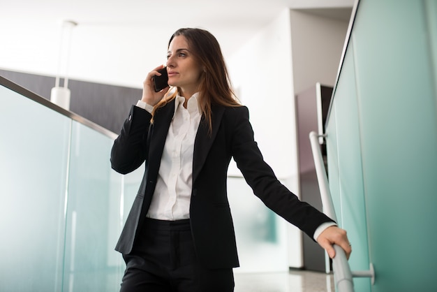 Donna di affari che parla al telefono mentre cammina giù per le scale nel suo ufficio