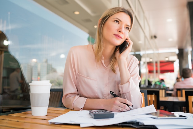 Donna di affari che parla sul telefono mentre lavorando alla caffetteria.