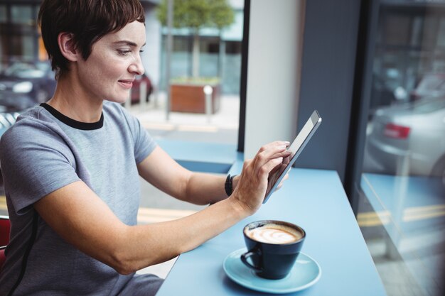 Donna di affari che per mezzo della compressa digitale mentre mangiando caffè