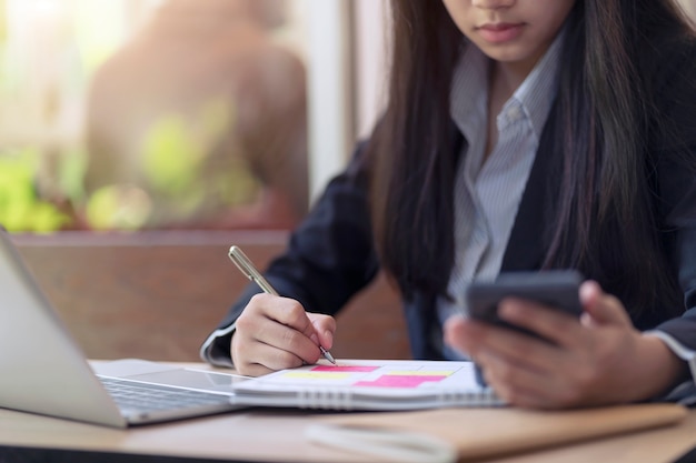 Donna di affari che scrive qualcosa idea nella nota sul calendario e che utilizza smartphone con calcolo