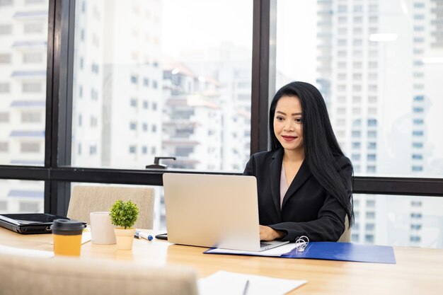 Donna di affari che si siede alla stazione di lavoro moderna luminosa e che digita sul computer portatile.