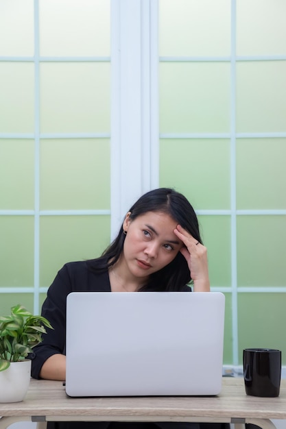 Donna di affari che si siede nella sedia della scrivania dell'ufficio con le mani che tengono la testa davanti al computer portatile