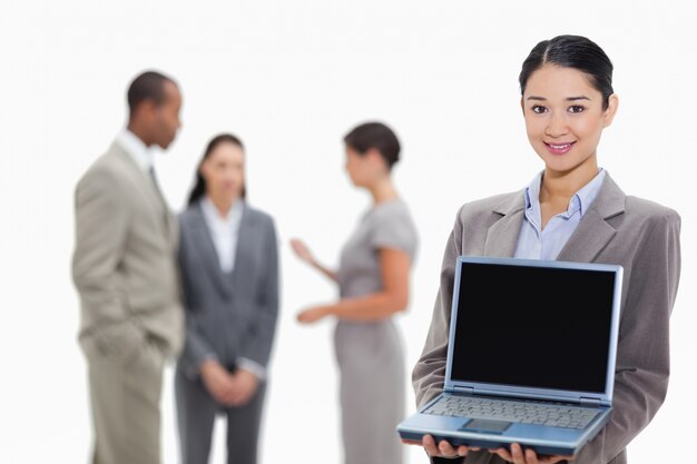 Donna di affari che sorride mostrando uno schermo del computer portatile con i colleghe nei precedenti