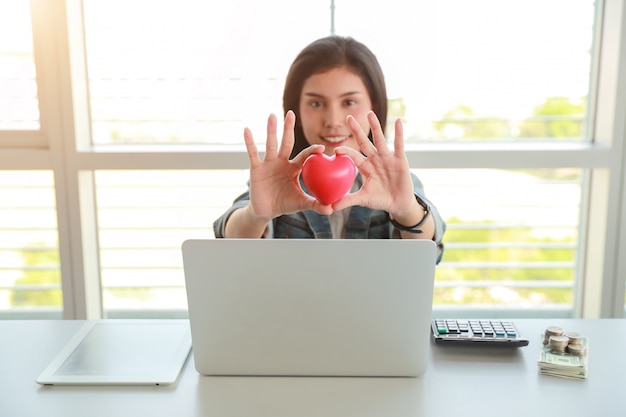 Donna di affari che tiene simbolo rosso del cuore sulla tavola con il computer