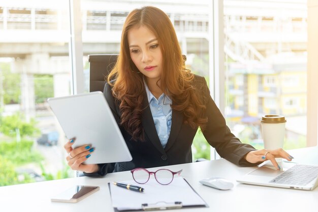 Donna di affari che utilizza cellulare con il computer portatile sullo scrittorio nell'ufficio.