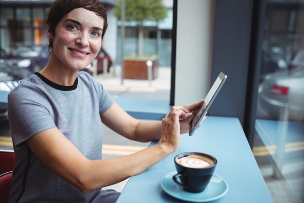 Donna di affari che utilizza compressa digitale mentre mangiando caffè nell'ufficio