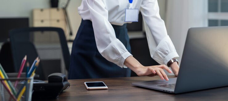 Donna di affari che utilizza computer portatile e smartphone con stazionario sulla tavola nell'ufficio.