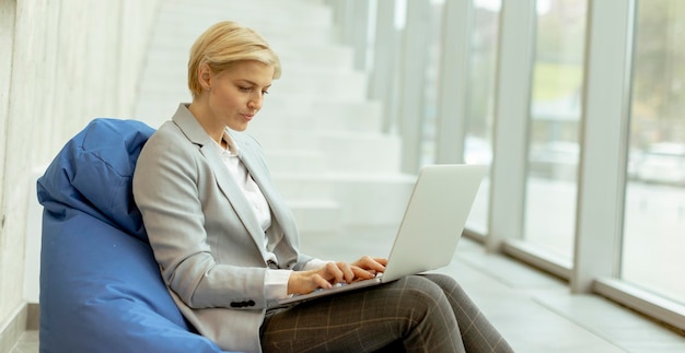 Donna di affari che utilizza il computer portatile sulla borsa pigra nell'ufficio moderno