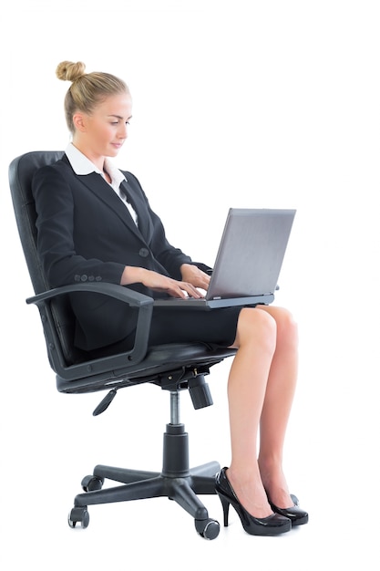 Donna di affari chic messa a fuoco che si siede su una sedia dell&#39;ufficio facendo uso del suo computer portatile