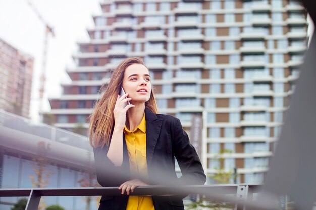 Donna di affari con un telefono cellulare nella via con gli edifici per uffici