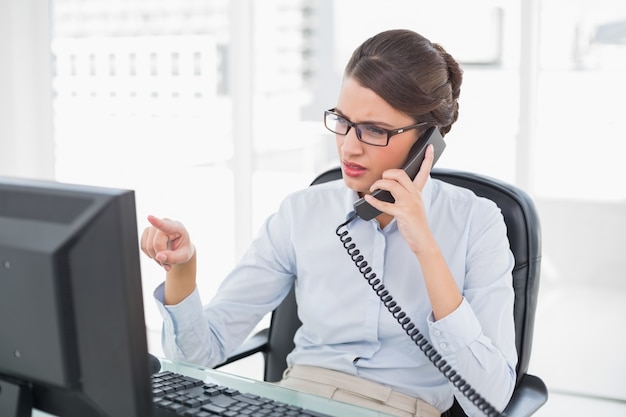 Donna di affari dai capelli marrone di classe aggrottante le sopracciglia che risponde al telefono