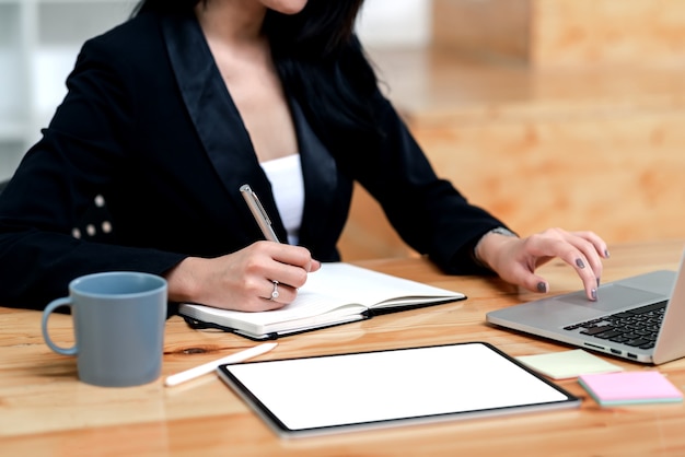 Donna di affari del primo piano che lavora con il computer portatile e che prende appunti all'ufficio.