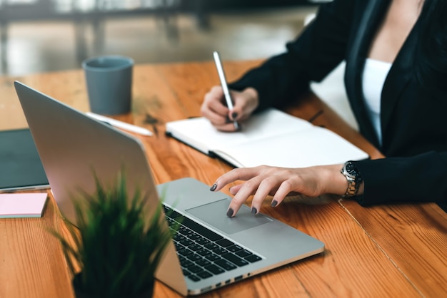 Donna di affari del primo piano che lavora con il computer portatile e che prende appunti all'ufficio.