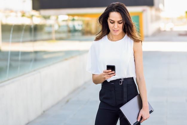 Donna di affari di mezza età che lavora con il suoi Smart Phone e computer portatile all&#39;aperto.