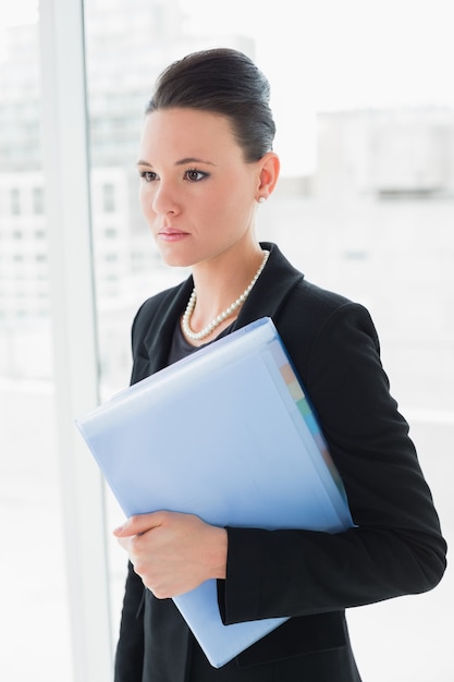 Donna di affari elegante che sta contro la parete di vetro dell&#39;ufficio con la cartella