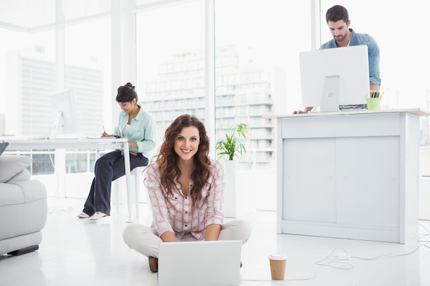 Donna di affari felice che si siede sul pavimento per mezzo del computer portatile