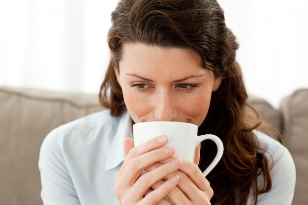 Donna di affari graziosa che beve caffè sul sofà