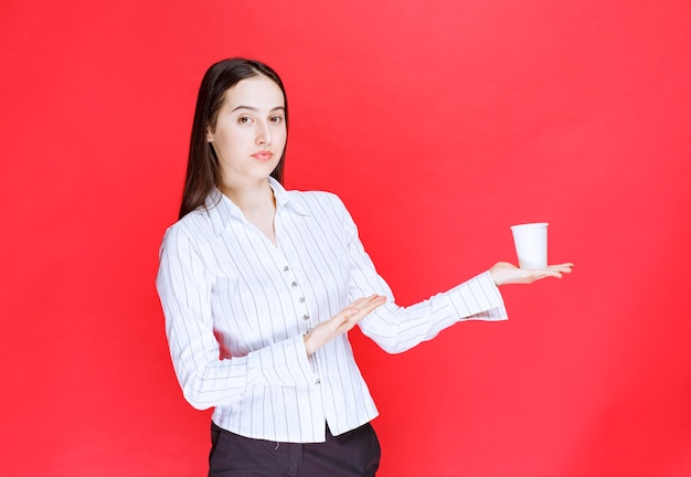 Donna di affari graziosa che posa con la tazza di plastica di tè su fondo rosso.