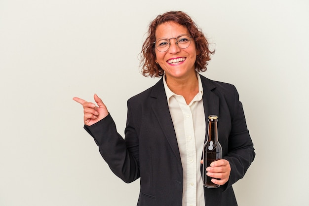 Donna di affari latina di mezza età che tiene una birra isolata su fondo bianco che sorride e che indica da parte, mostrando qualcosa allo spazio vuoto.