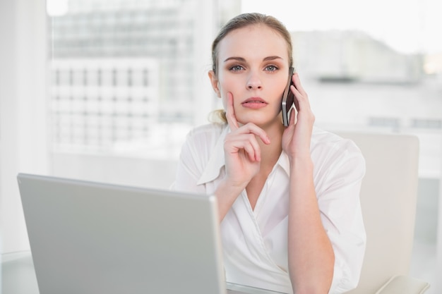 Donna di affari premurosa che per mezzo del computer portatile e facendo una chiamata che esamina macchina fotografica