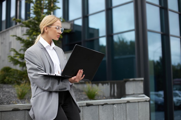 Donna di affari seria che utilizza il computer portatile digitando sulla tastiera lavorando online per strada