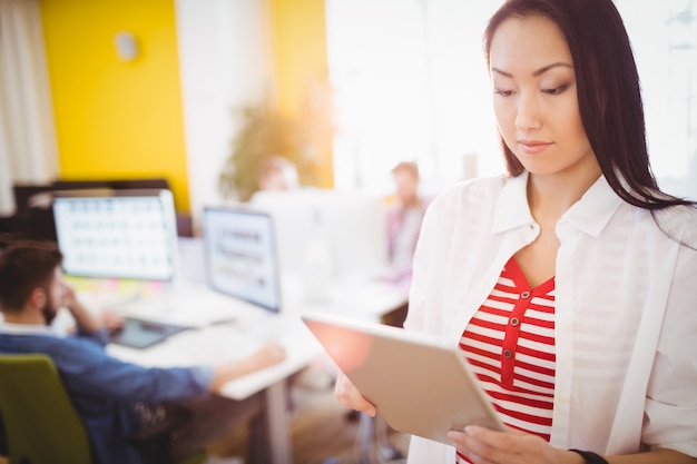 Donna di affari sicura che per mezzo della compressa digitale all'ufficio creativo