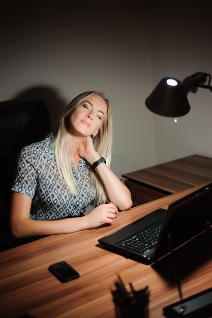 Donna di affari sollecitata che si siede alla scrivania e che pensa alla soluzione mentre lavorando tardi davanti ad un computer.