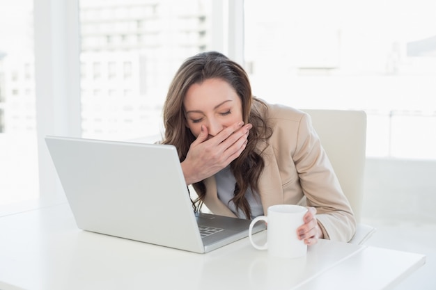 Donna di affari sonnolenta che sbadiglia davanti al computer portatile all&#39;ufficio