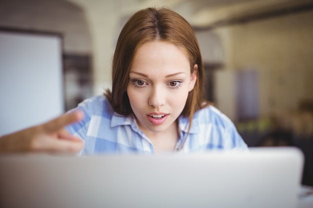 Donna di affari sorpresa che lavora al computer portatile in ufficio