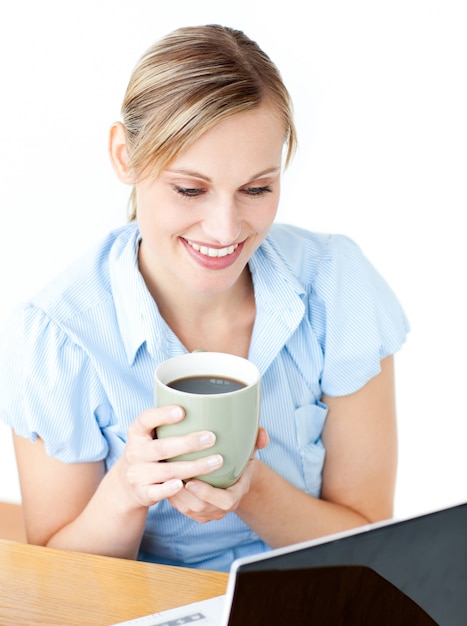 Donna di affari sorridente che beve caffè facendo uso del suo computer portatile