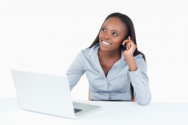 Donna di affari sorridente che fa una telefonata mentre per mezzo di un computer portatile