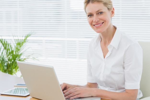 Donna di affari sorridente che per mezzo del computer portatile allo scrittorio