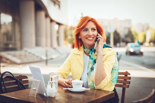 Donna di affari sorridente che utilizza il telefono durante una pausa caffè in un caffè di strada.