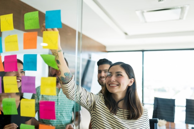 Donna di affari sorridente ispanica che fa brainstorming sopra le note adesive nella riunione