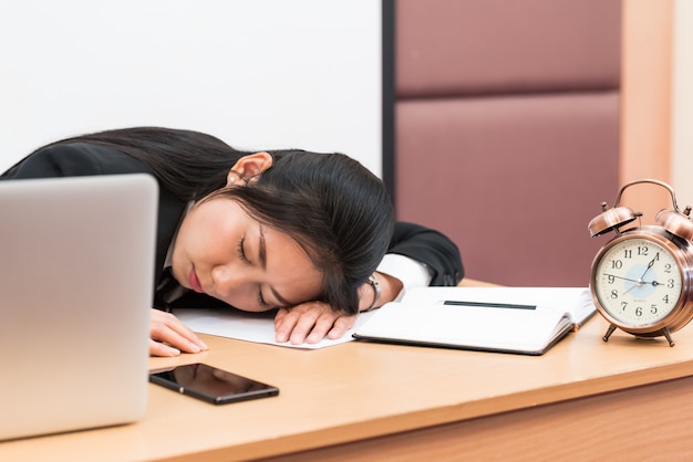 Donna di affari sovraccaricata e stanca che dorme sopra una scrivania sul lavoro nel suo ufficio.