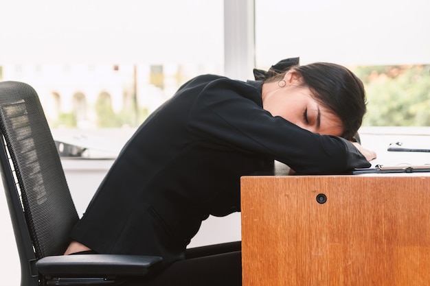 Donna di affari stanca che dorme con il computer portatile sulla tavola all&#39;ufficio