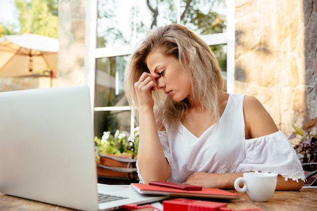 Donna di affari stanca che lavora con il computer portatile, mentre sedendosi al caffè, all'aperto