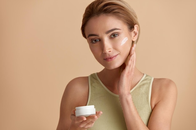 Donna di bellezza che applica la crema per il viso Primo piano del modello femminile che tiene la bottiglia di crema