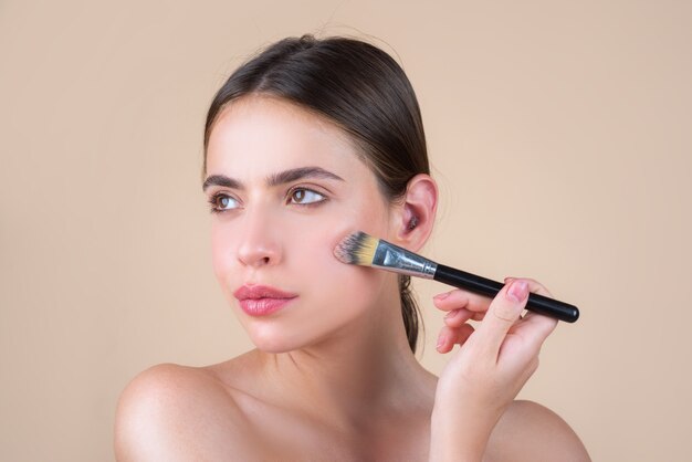 Donna di bellezza con trucco naturale, modello di bellezza fresca con pennello per il trucco. Bellissimi cosmetici per il benessere femminile. Concetto di cura della pelle della stazione termale. Trattamento facciale.